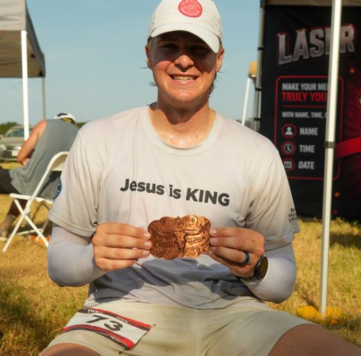 Pierce Showe holding a 100-mile ultramarathon finisher belt buckle