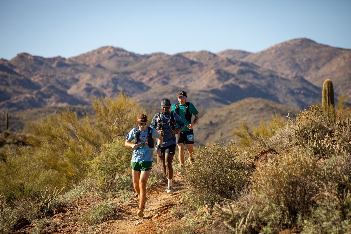 Runners on the desert singletrack of the Black Canyon Trail with saguaros and mountains behind them