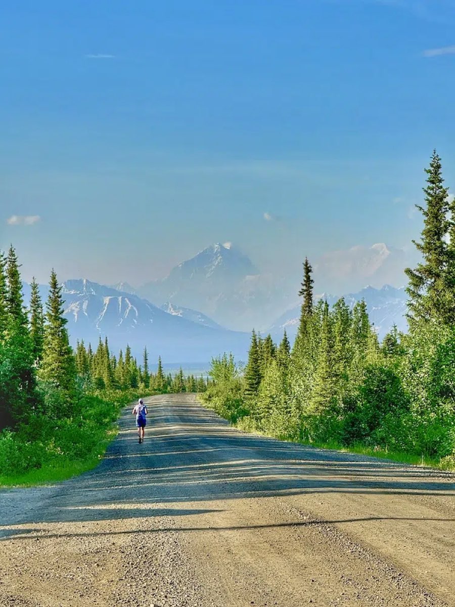 A runner on the gravel Denali Highway in Alaska with snow-capped Alaska Range peaks ahead
