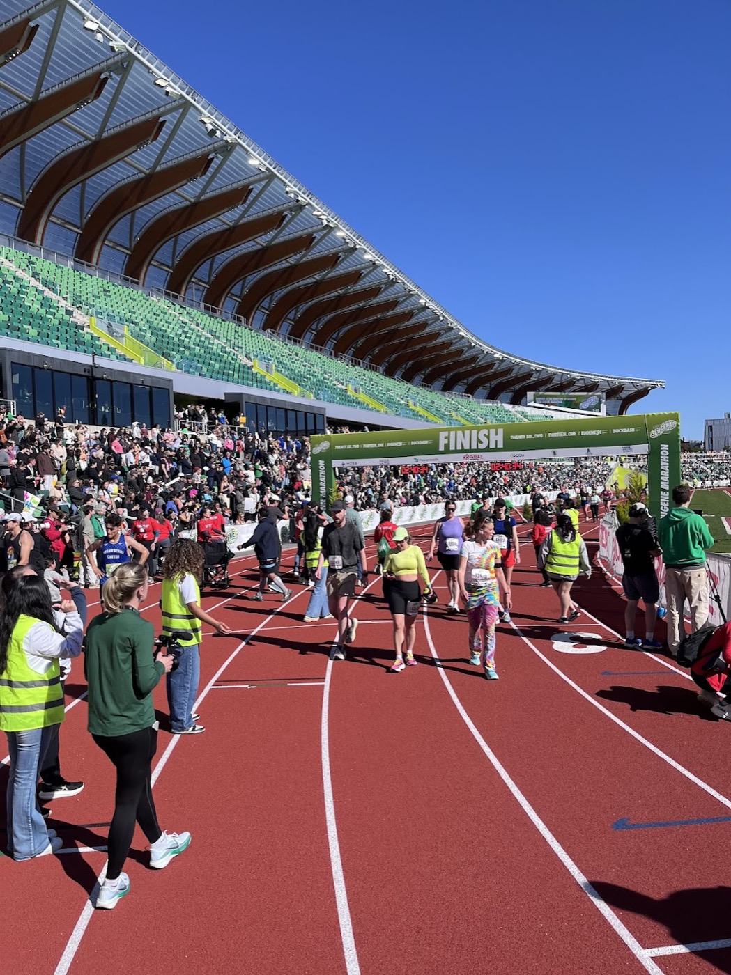 Runners on the red track approaching the finish arch inside Hayward Field at the Eugene Marathon
