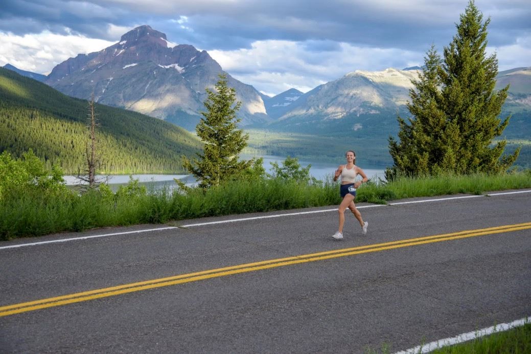 A runner on the Glacier Half Marathon course with a lake and mountains behind her