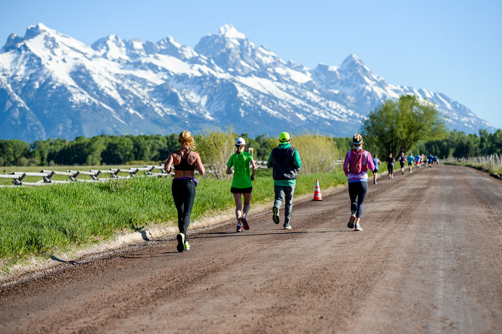 Runners on a dirt road toward the snow-capped Teton Range
