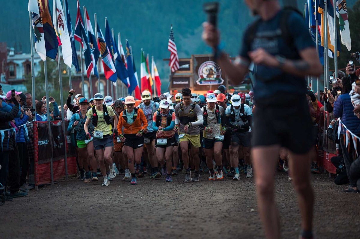Runners starting the Hardrock 100 in Silverton, Colorado, between rows of flags and spectators