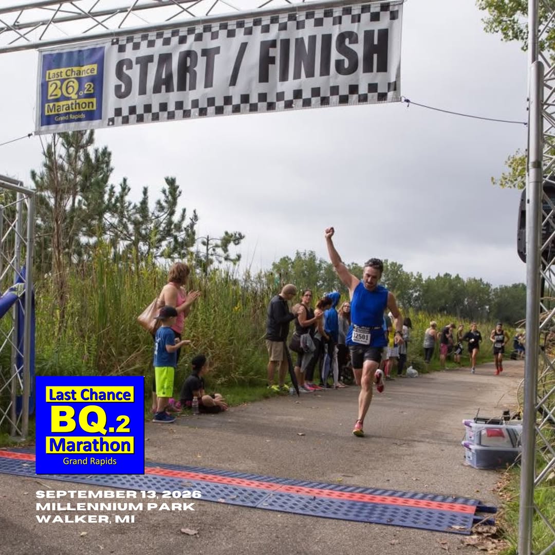 A runner raising his fist as he crosses under the Last Chance BQ.2 Marathon start and finish banner in Millennium Park