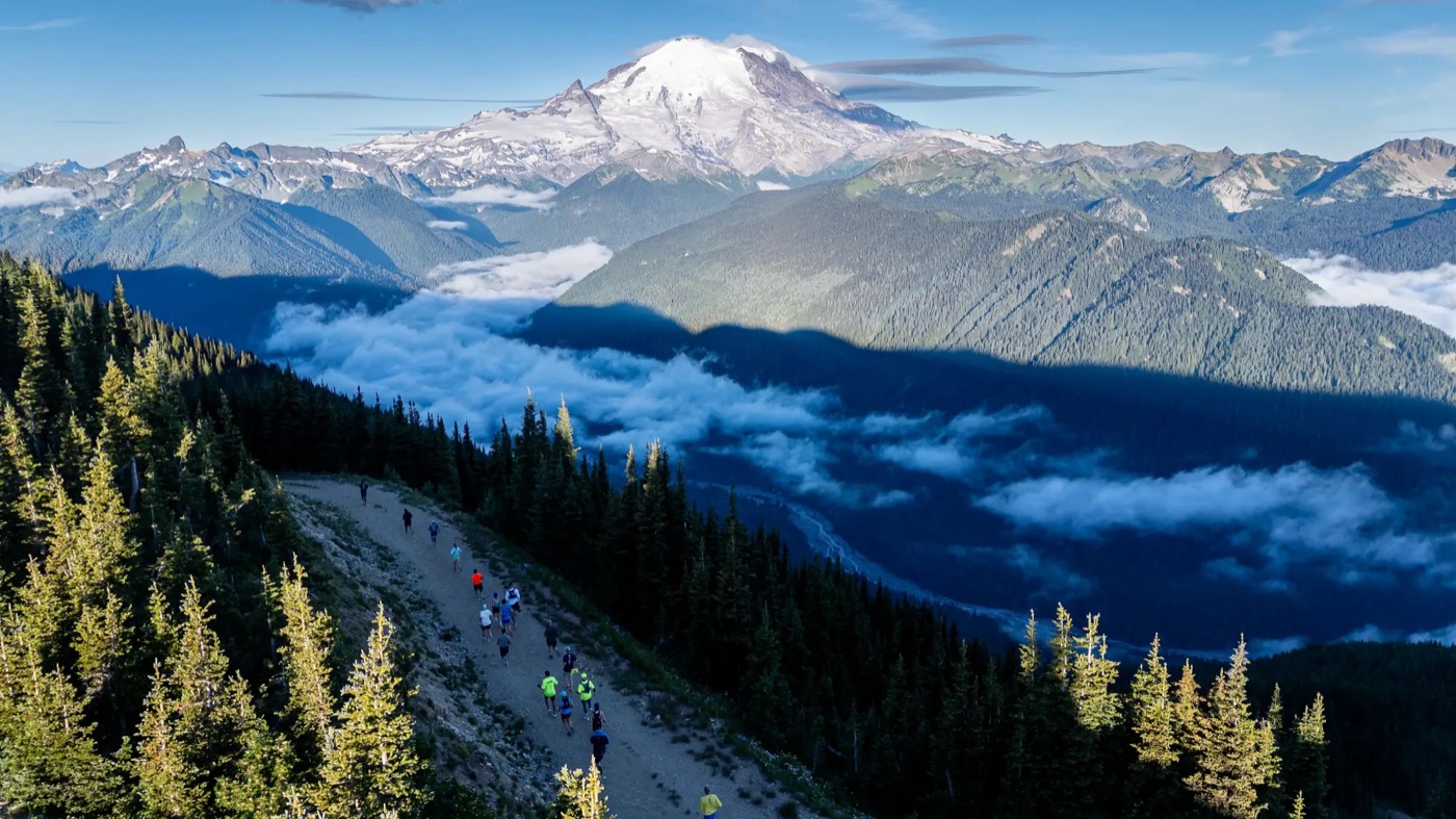 Runners on a ridgeline trail with Mount Rainier behind them