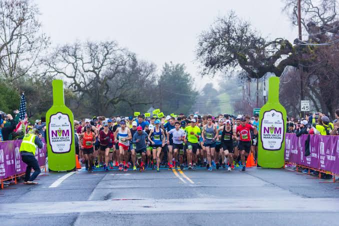 Runners leaving the Napa Valley Marathon start line between two giant inflatable wine bottles