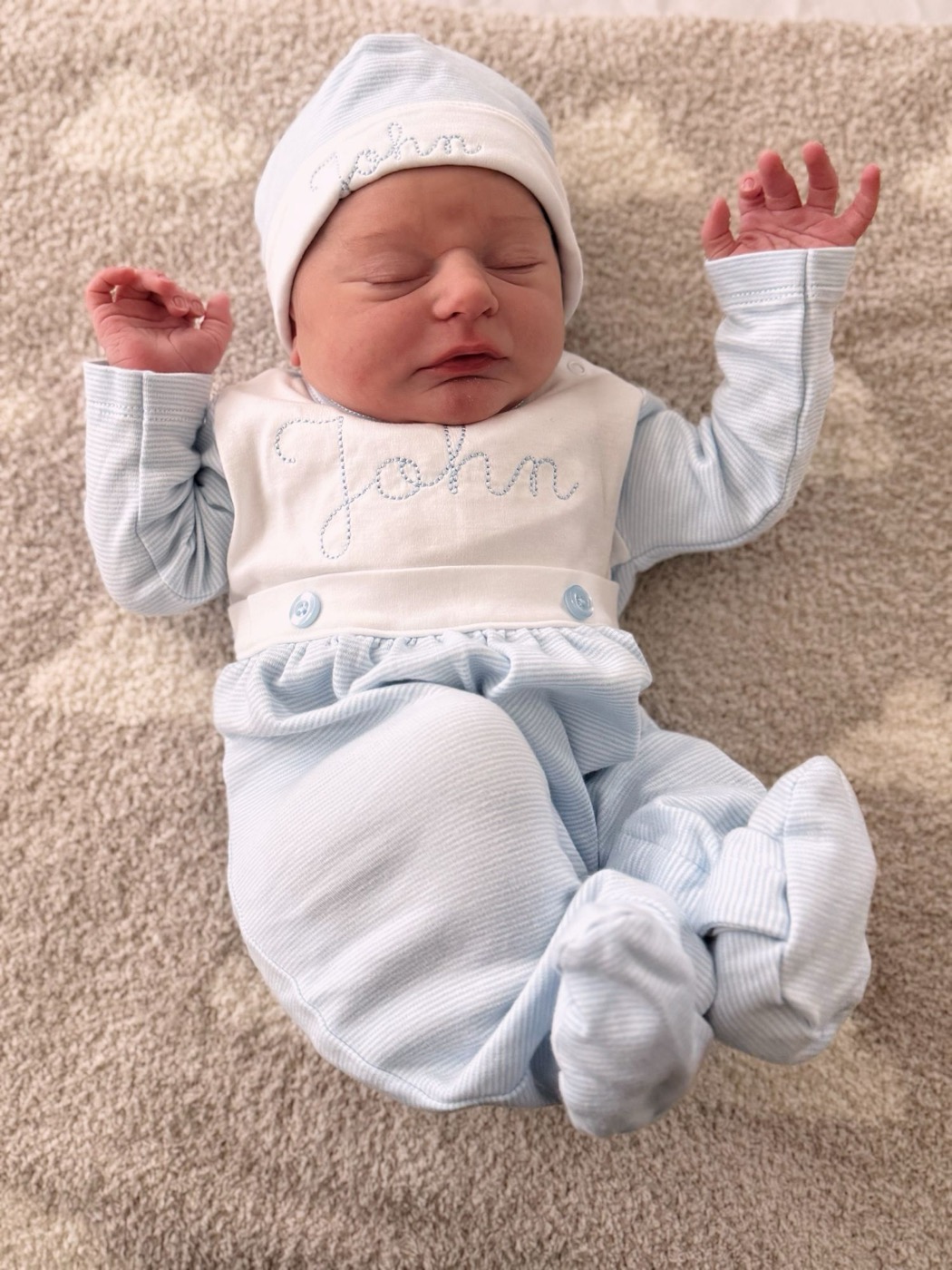Newborn John asleep in a light blue outfit and hat embroidered with his name