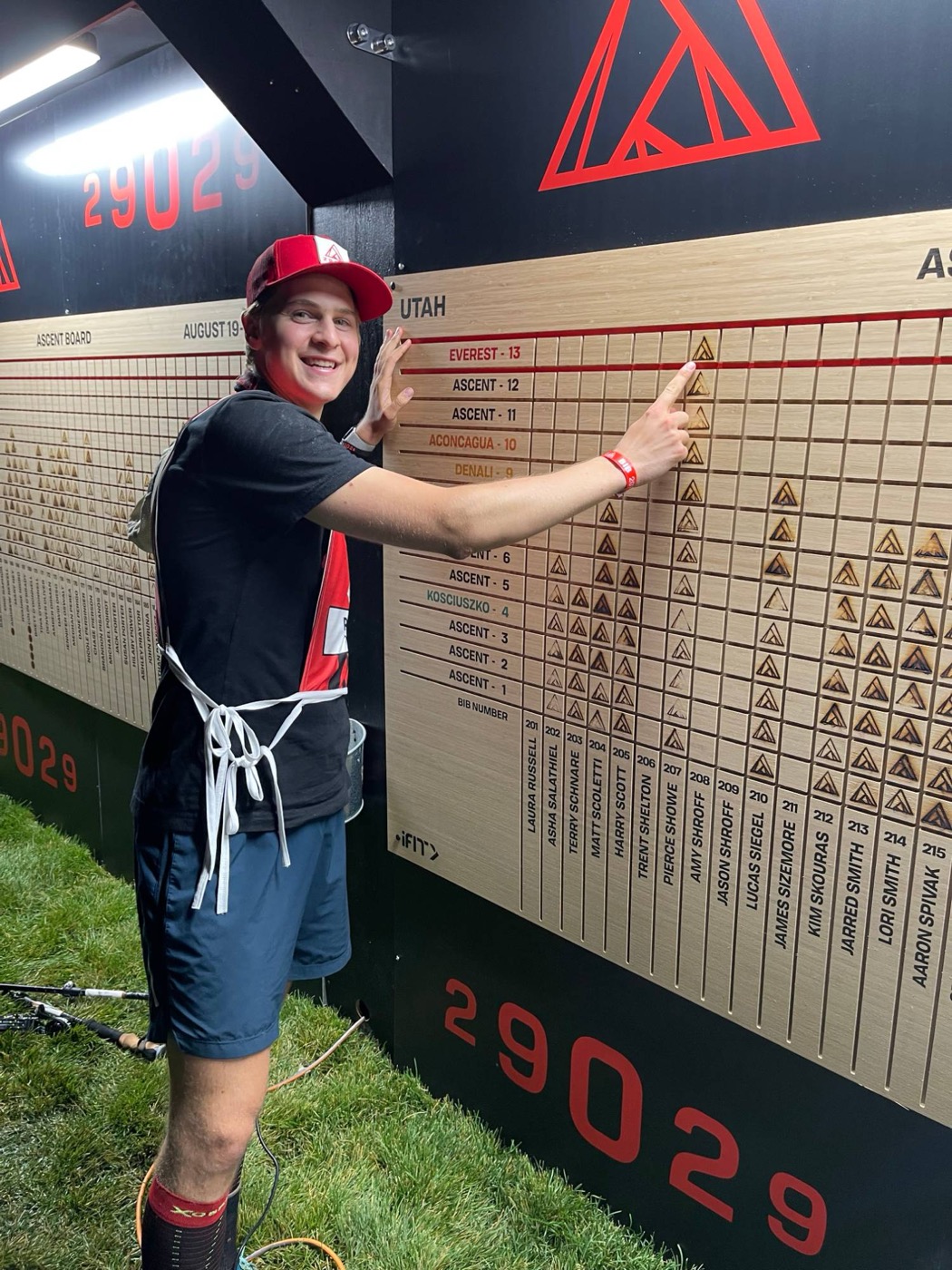 Pierce Showe smiling and pointing to the Everest row on the 29029 ascent board at Snowbasin
