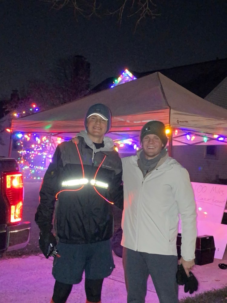 Pierce Showe at night during his first 100-mile run, wearing a light-up safety vest beside a pop-up tent decorated with Christmas lights