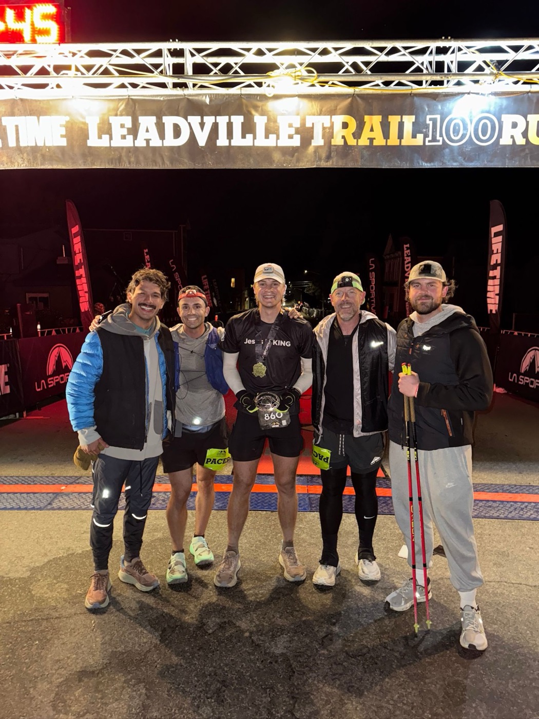 Pierce Showe at night under the 2025 Leadville Trail 100 finish banner with his medal and buckle, standing with four crew members and pacers