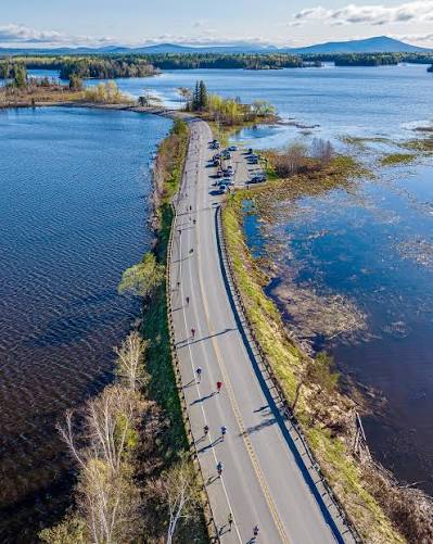 Aerial view of marathon runners on a two-lane road crossing between lakes in western Maine
