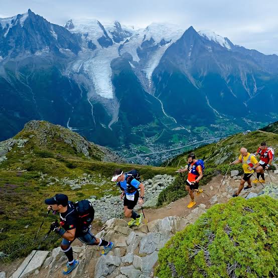 UTMB runners climbing a rocky trail above the Chamonix valley with Mont Blanc's glaciers behind