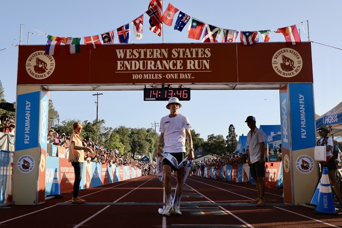 A runner finishing the Western States Endurance Run under the finish arch on the track in Auburn, California