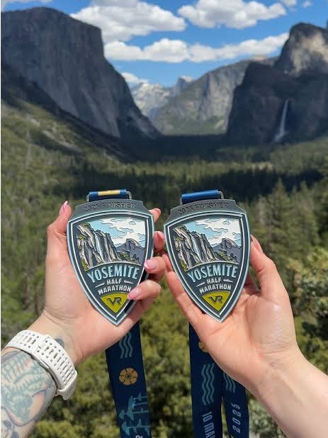Two Yosemite Half Marathon finisher medals held up at Tunnel View