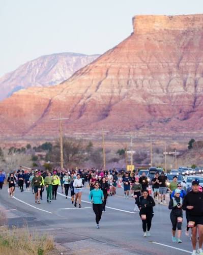 A crowd of runners on the Zion Half Marathon course with red cliffs behind them